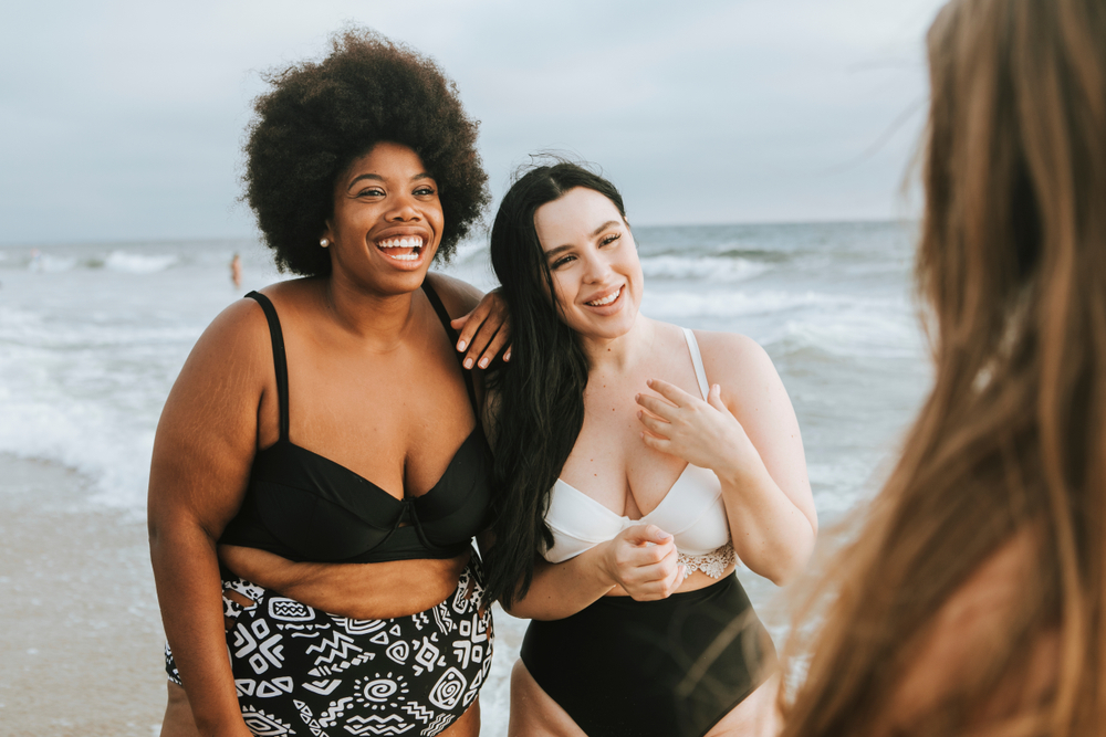 Two women in bikinis stand together talking to a third woman about the importance of self-confidence