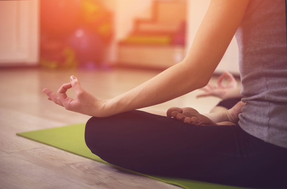Close up hands. Girl do yoga indoors. Woman exercising yoga at sunset with a warmth background in gym. Young woman conducts meditating indoors.