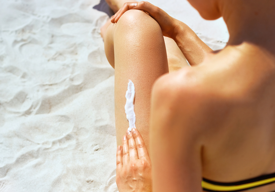 Closeup on female Hand applying sunscreen creme on Leg. Skincare. Sun protection sun cream, on her smooth tanned legs.