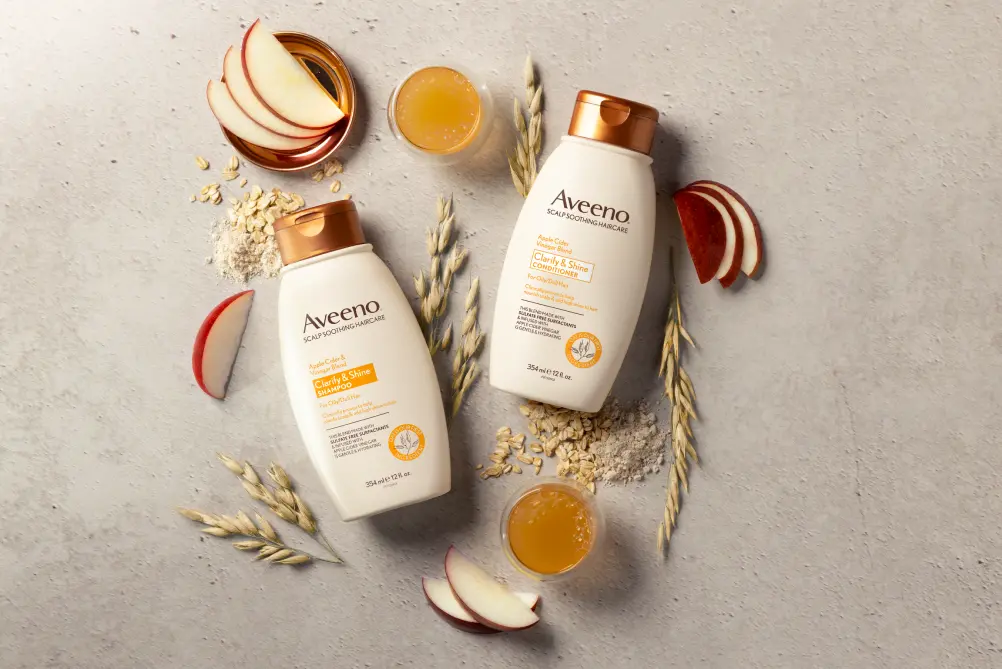 Set of Aveeno® Clarity & Shine Shampoo and Conditioner surrounded by nourishing hair ingredients