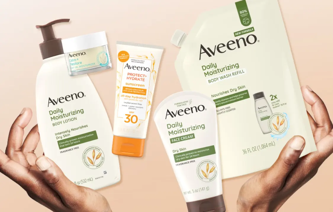 A pair of hands holding five different Aveeno products