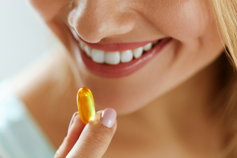 A woman takes a fish oil capsule to reap omega-3 benefits for skin.