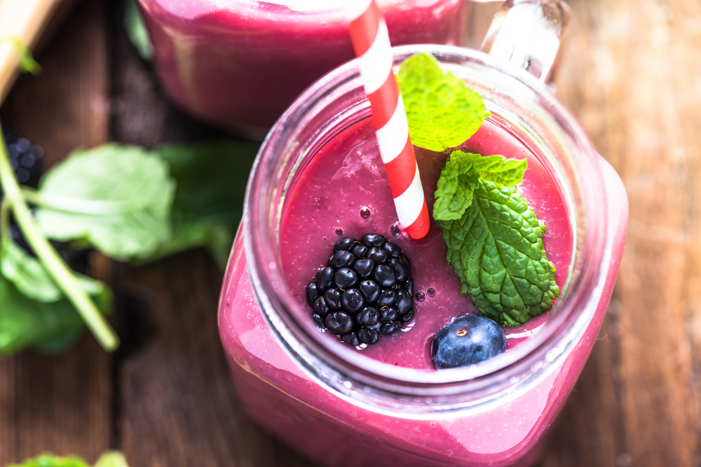 A red-pink smoothie topped with berries sits in a glass mason jar mug.